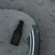 100% Organic and All Natural Face & Body Oil Featuring Black Seed Oil – BLOOM – Scent of Spring Blossoms packaged in 30ml Amber Glass Bottle pictured from above lying on a surfboard covered with a thin layer of sand - Non Greasy, Multi-Purpose, Fast Absorbing, Vegan Friendly, Nutrient Dense, Eco-friendly, Sustainable, Waterless and Unisex Skincare Oils made by Oasis Black – Organic Botanical Skincare - Born in Morocco, Made in small handmade batches in the Byron Bay region