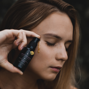 100% Organic and All Natural Face & Body Oil Featuring Black Seed Oil – BLOOM – Scent of Spring Blossoms packaged in 30ml Amber Glass Bottle with Natural Golden Mica pictured being dropped like liquid gold onto the face of a woman - Non Greasy, Multi-Purpose, Fast Absorbing, Vegan Friendly, Nutrient Dense, Eco-friendly, Sustainable, Waterless and Unisex Skincare Oils made by Oasis Black – Organic Botanical Skincare - Born in Morocco, Made in small handmade batches in the Byron Bay region