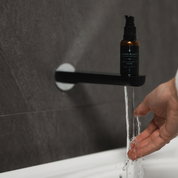 100% Organic and All Natural Face & Body Oil Featuring Black Seed Oil – BYRON – Scent inspired by Byron Bay packaged in 30ml Amber Glass Bottle pictured resting on top of a tap with water running into a bath - Non Greasy, Multi-Purpose, Fast Absorbing, Vegan Friendly, Nutrient Dense, Eco-friendly, Sustainable, Waterless and Unisex Skincare Oils made by Oasis Black – Organic Botanical Skincare - Born in Morocco, Made in small handmade batches in the Byron Bay region
